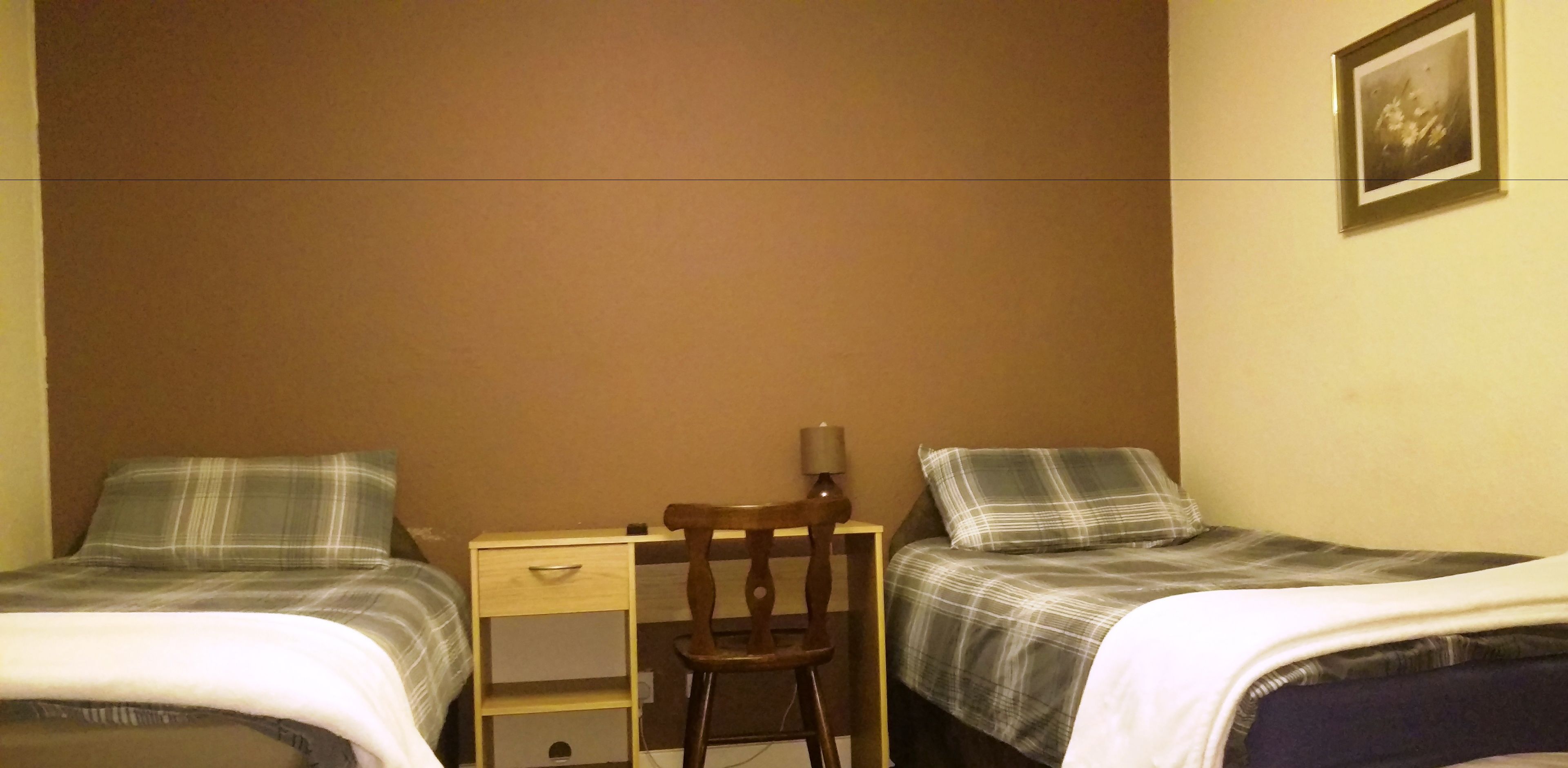 Ein Schlafzimmer mit zwei Betten, einem hölzernen Stuhl, einem kleinen Schreibtisch und einer Lampe.