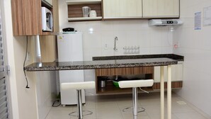 Una cocina compacta con microondas, cafetera y horno empotrado. Hay dos taburetes blancos y un lavamanos pequeño.