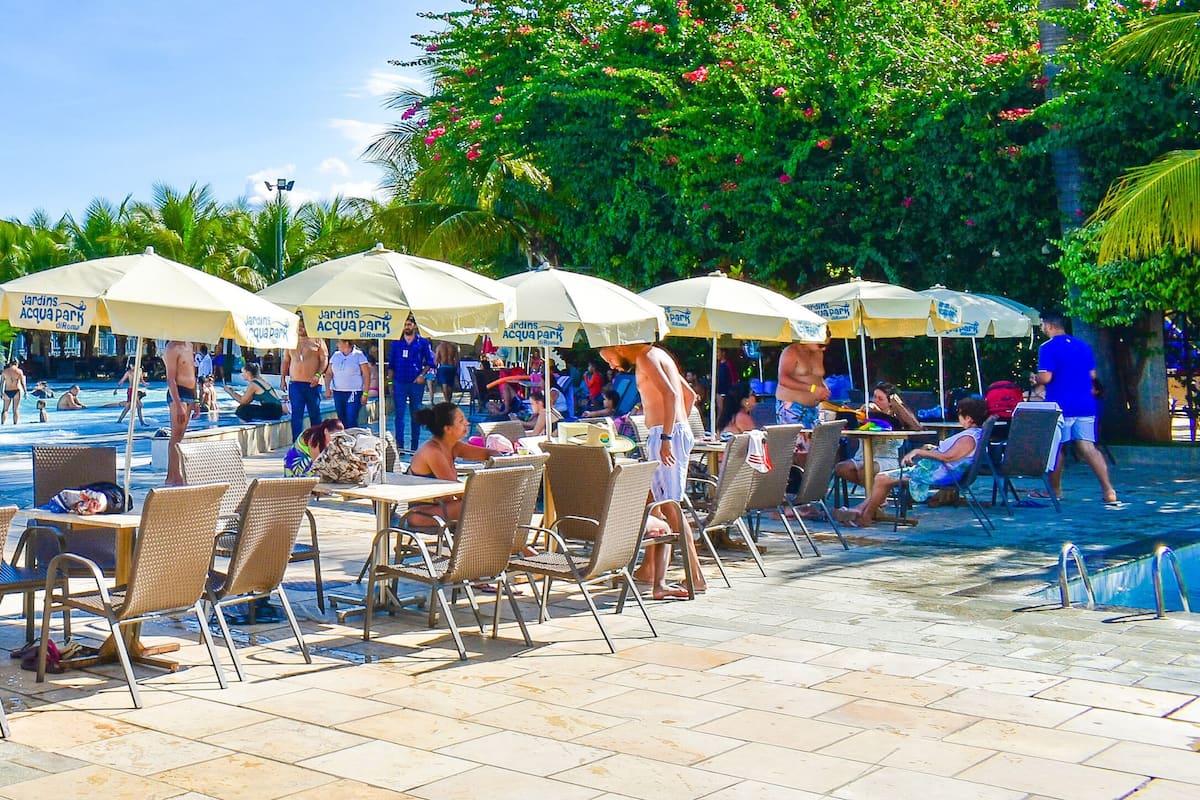 A poolside area with lounge chairs and umbrellas, a swimming pool, and palm trees in the background.