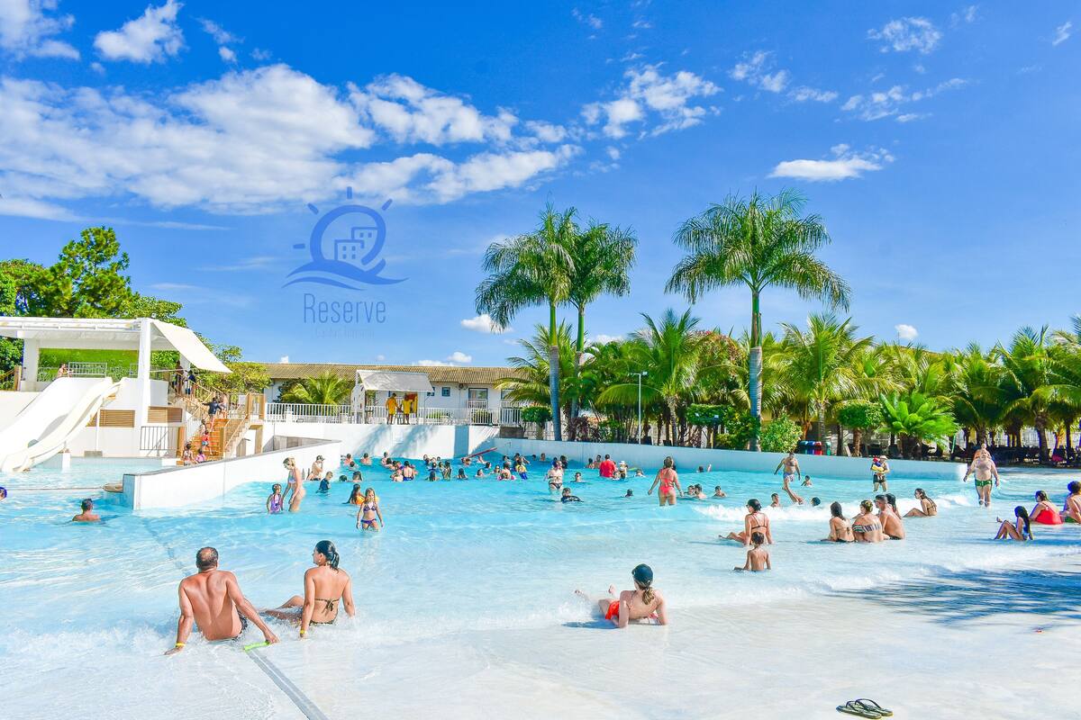 A large outdoor swimming pool with multiple lanes, palm trees, and a water slide.
