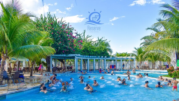Un área de piscina con varias piscinas, palmeras y una zona de estar cubierta.