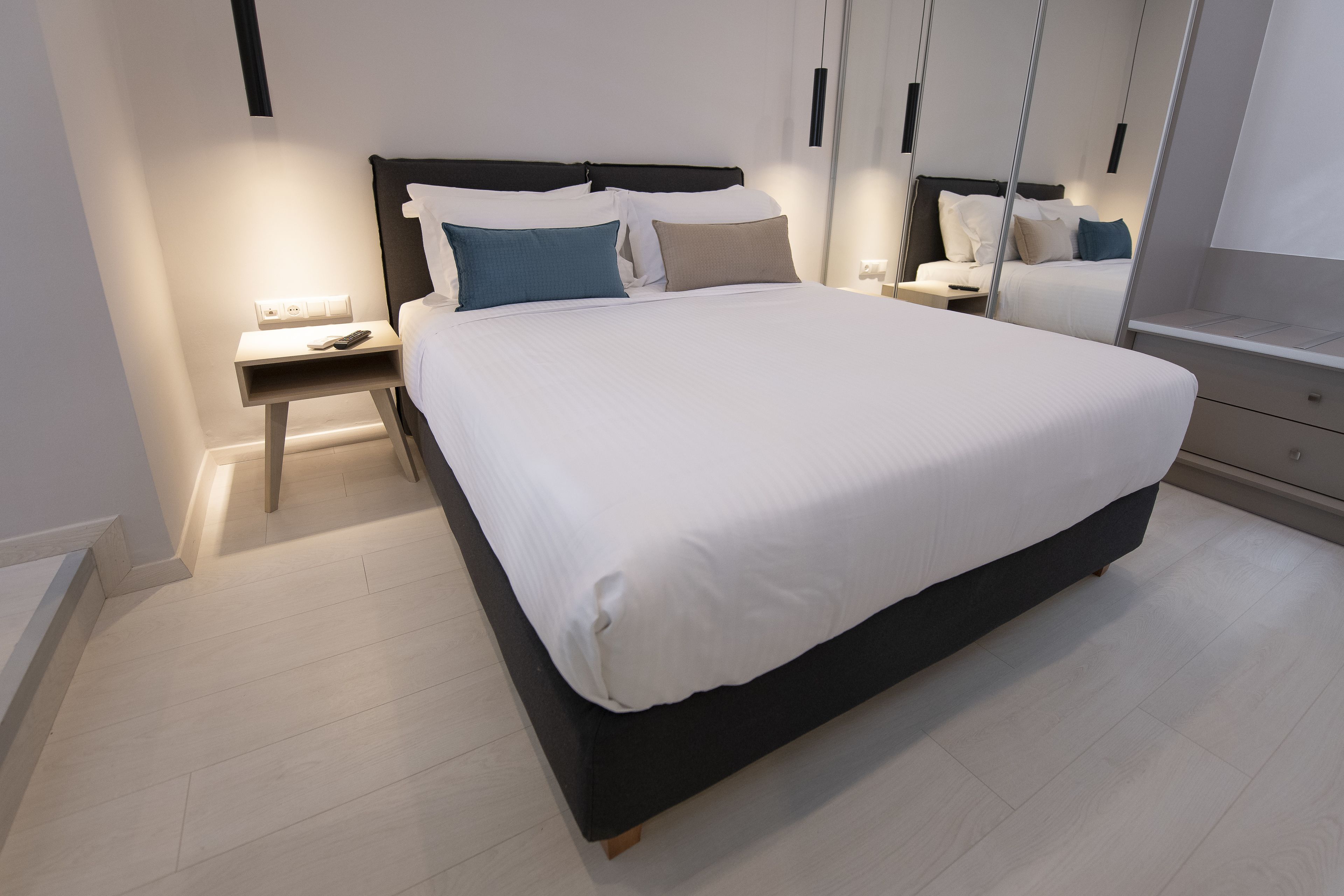 A modern bedroom with a large bed, bedside tables, a mirror, and a wardrobe.