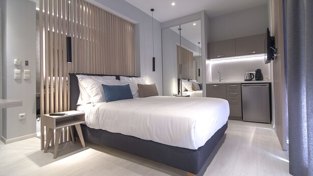 A modern bedroom with a large bed, bedside tables, a built-in wardrobe, and a kitchenette area. - Acropolis Stay (Athens)
