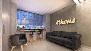 A modern living area with a sofa, two chairs, a bar counter, and a large window. - Acropolis Stay (Athens)