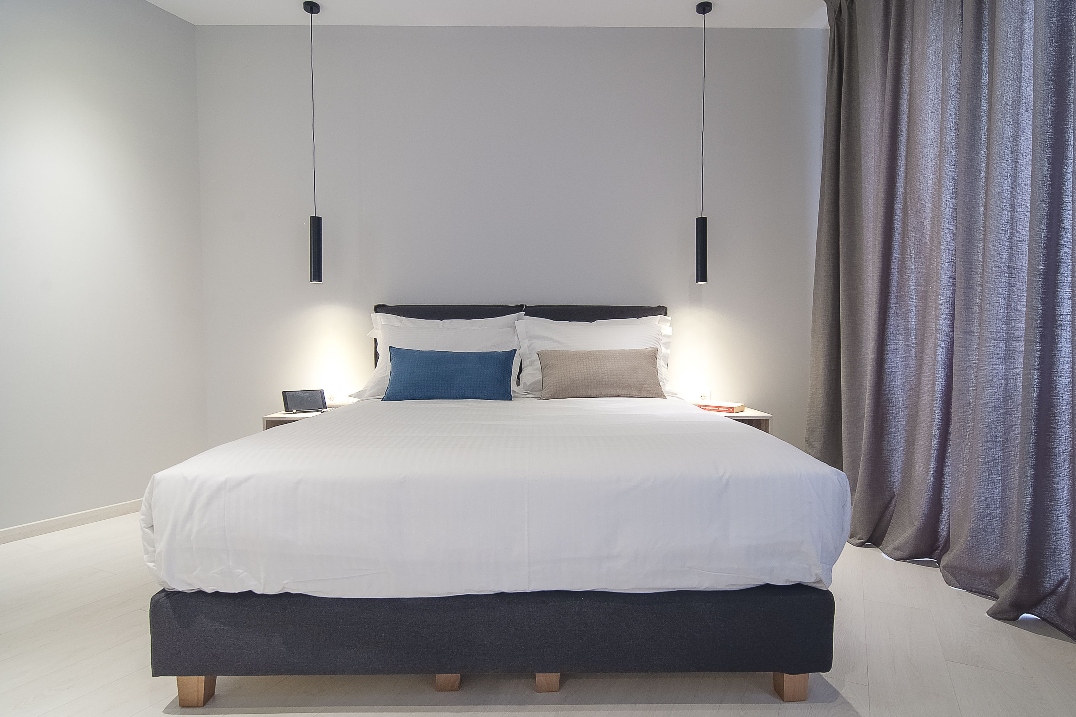 A modern bedroom with a large bed, bedside tables, and a hanging light fixture.