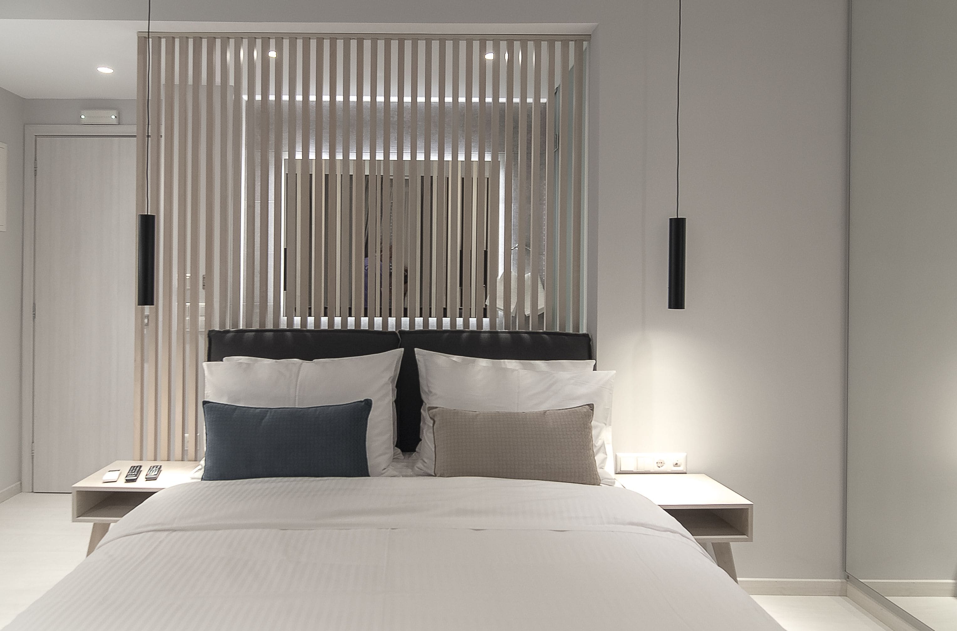 A modern bedroom with a large bed, two bedside tables, and a headboard with vertical blinds.
