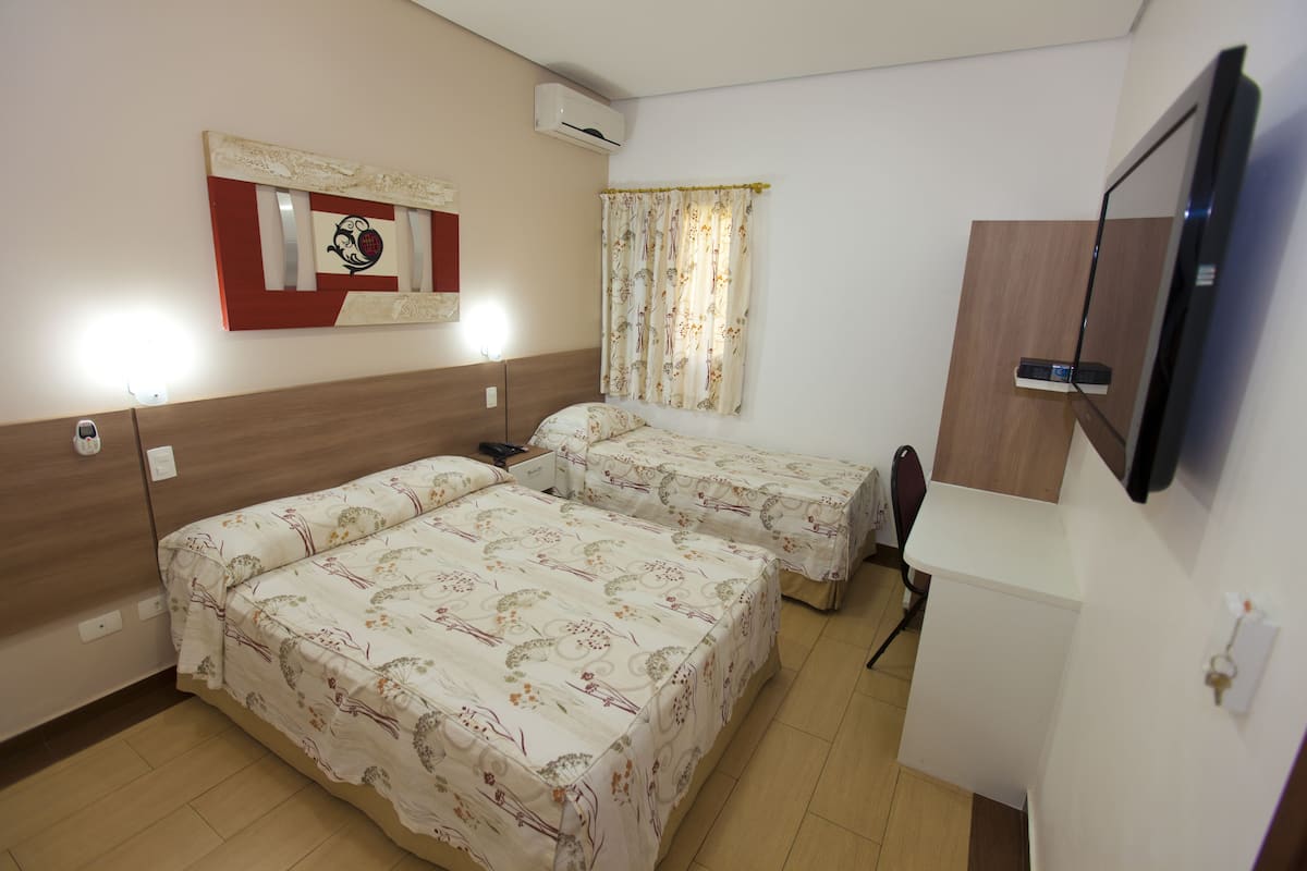 Une chambre d’hôtel avec deux lits, une télévision, un miroir et un climatiseur fixé au mur.