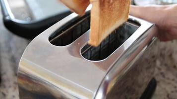 A hand holding a slice of toast over a toaster.