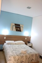 Una cama bien hecha con colcha de estampado floral, cabecera de madera y una obra de arte colgada en la pared.