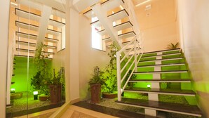 Escadaria moderna com guarda-corpos de vidro e detalhes em verde, cercada por plantas em vasos e um piso espelhado.