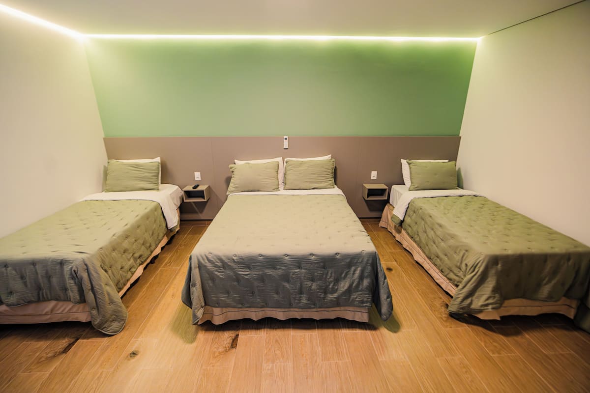 Une chambre avec trois lits simples, un mur d’accent de couleur verte et un plancher en bois.