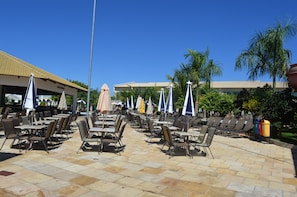An outdoor patio area with tables and chairs, umbrellas, and palm trees. - Reserva Caldas Lacqua 2 (Caldas Novas)