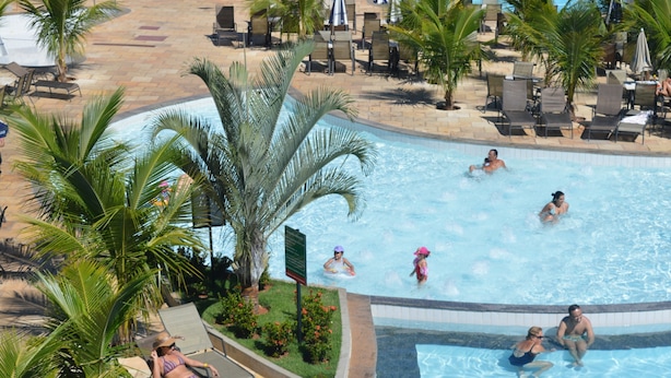 Un área de piscina con sillas de descanso, palmeras y una piscina con azulejos.