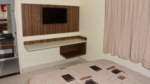 Un dormitorio con televisor integrado, repisa de madera, alfombra estampada y ventana con cortinas.