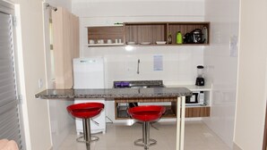 Una cocina compacta con encimera de granito, dos taburetes rojos, un refrigerador, un microondas y una cafetera.
