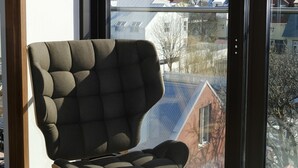 Een moderne stoel in een kamer met een groot raam dat uitkijkt op een gebouw met een puntige toren.