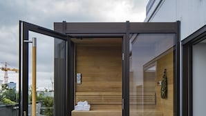 Een moderne buitenruimte met een houten bank, een rieten stoel en een glazen deur naar een gebouw.