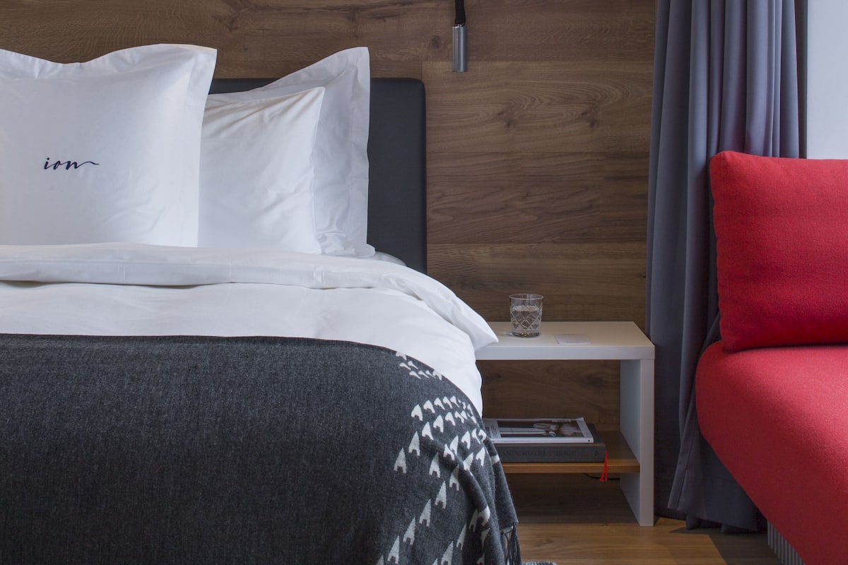 A modern bedroom with a wooden headboard, a bedside table with a lamp, a red chair, and a bedside table with a glass.
