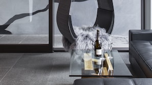 Een modern interieur met een hangstoel, een glazen tafel met een fles en glas, en een bank.