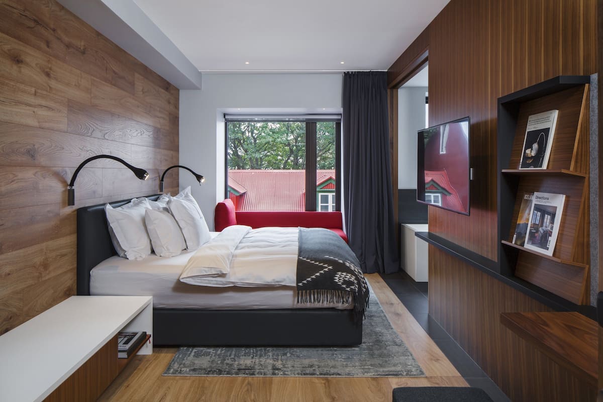 A modern bedroom with a large bed, wooden paneling, a red sofa, a TV, and a bookshelf.
