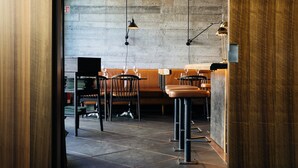 Een restaurant met hoge krukken, een lange bank, een betonnen muur en hangende吊灯.