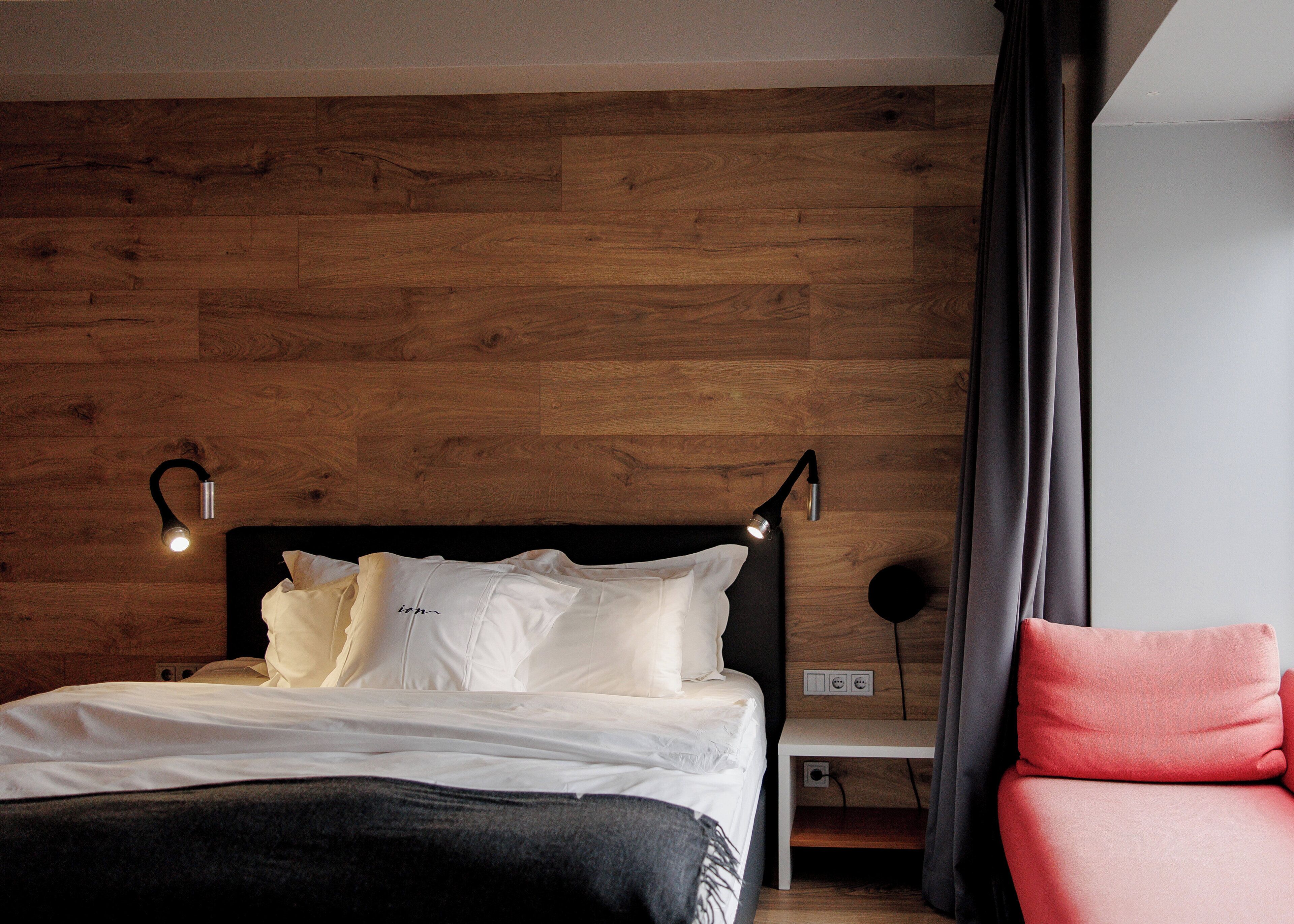 Ein Schlafzimmer mit einer Holzwand, einem Bett mit weißer Bettwäsche, zwei Nachttischlampen, einem Nachttisch und einem roten Sessel.