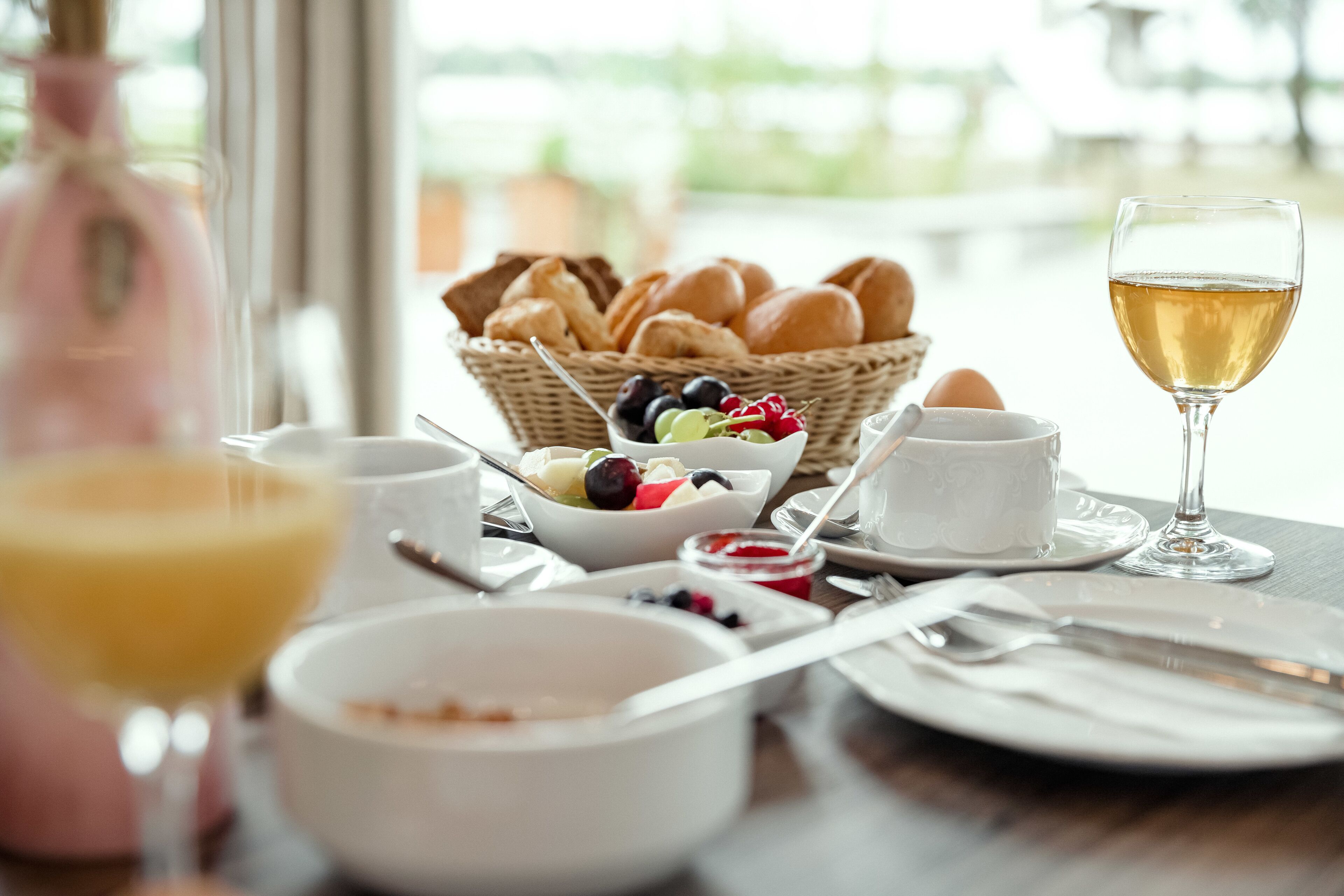 A breakfast setting with bread, fruits, and a glass of wine on a table.
