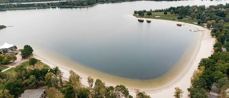 An aerial view of a lake with a sandy beach, surrounded by trees and a few buildings.