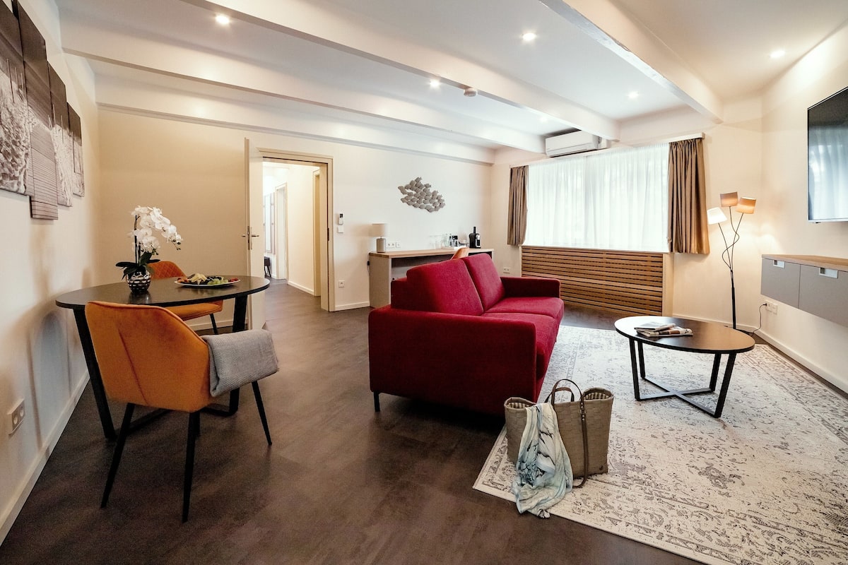 A modern living room with a red sofa, a dining table with chairs, and a small side table.