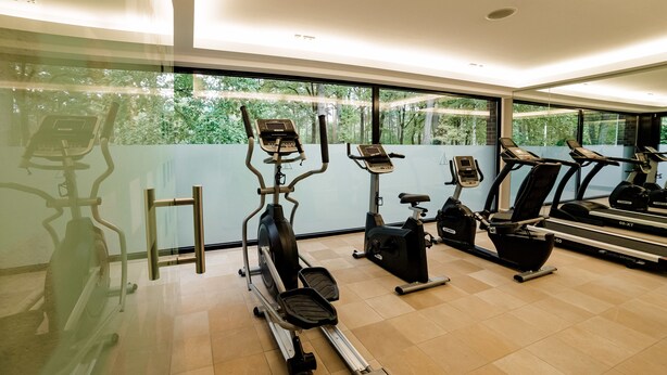 A modern gym with various cardio machines, large windows, and a clean, tiled floor. - Seehotel am Tankumsee (Isenbuttel)