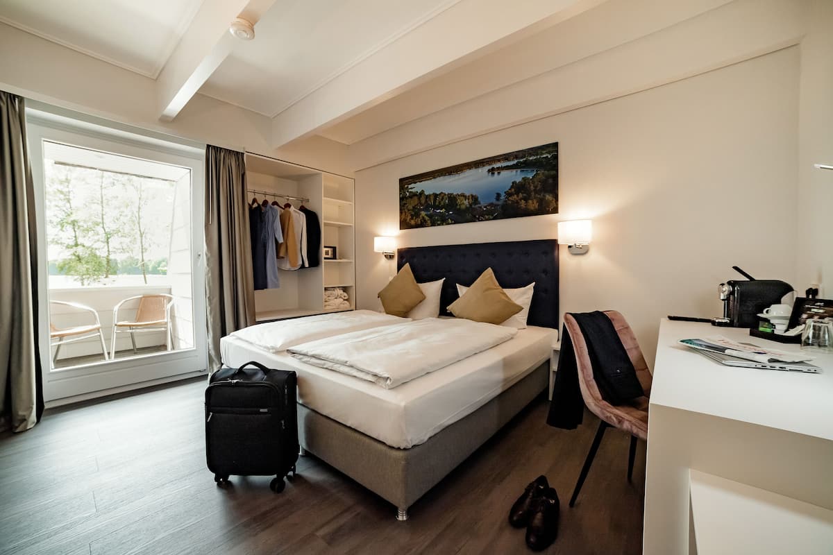 A hotel room with a bed, a desk, a chair, a suitcase, and a view of the outdoors.