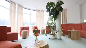 Un vestíbulo moderno con asientos rojos, mesas de madera y plantas en macetas.