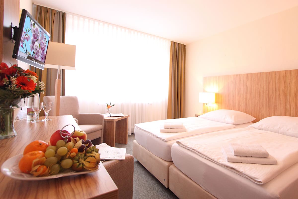 Une chambre d’hôtel avec deux lits, un bureau avec un ordinateur portable, une télévision et un panier de fruits.