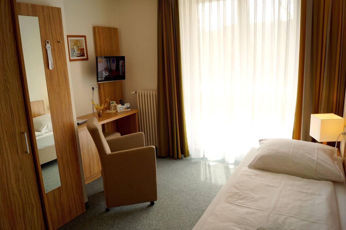 Une chambre d’hôtel avec un lit, un bureau, une chaise, une télévision et une fenêtre avec des rideaux.