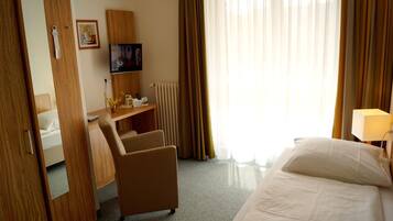 A hotel room with a bed, a desk, a chair, a TV, and a window with curtains.