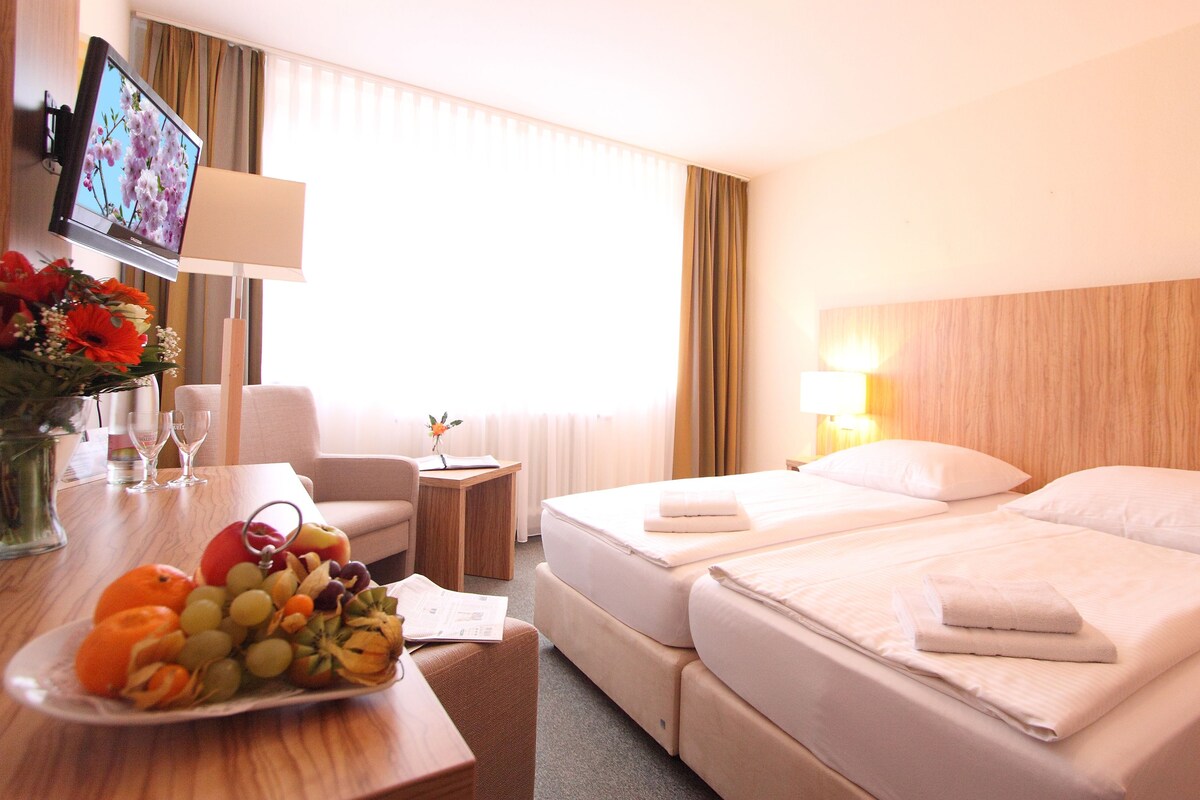 Habitación de hotel con dos camas, un escritorio con una computadora portátil, un televisor y un frutero.