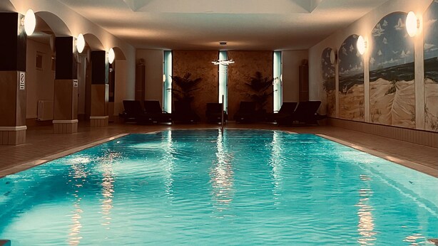 Una piscina interior con agua cristalina, tragaluces e iluminación en la pared.