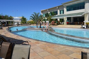 A swimming pool with multiple lanes, lounge chairs, and a building with large windows and a covered patio area.