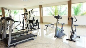A gym with cardio machines, weight equipment, and a large window with a view of palm trees. - Reserva Caldas Lacqua 3 (Caldas Novas)