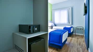 Quarto compacto com cozinha compacta, cama com roupa de cama azul, janela com cortinas e uma pequena mesa.