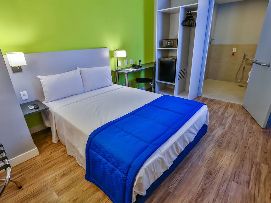 Habitación de hotel con cama, mesitas de noche, escritorio, zona de ducha y armario.