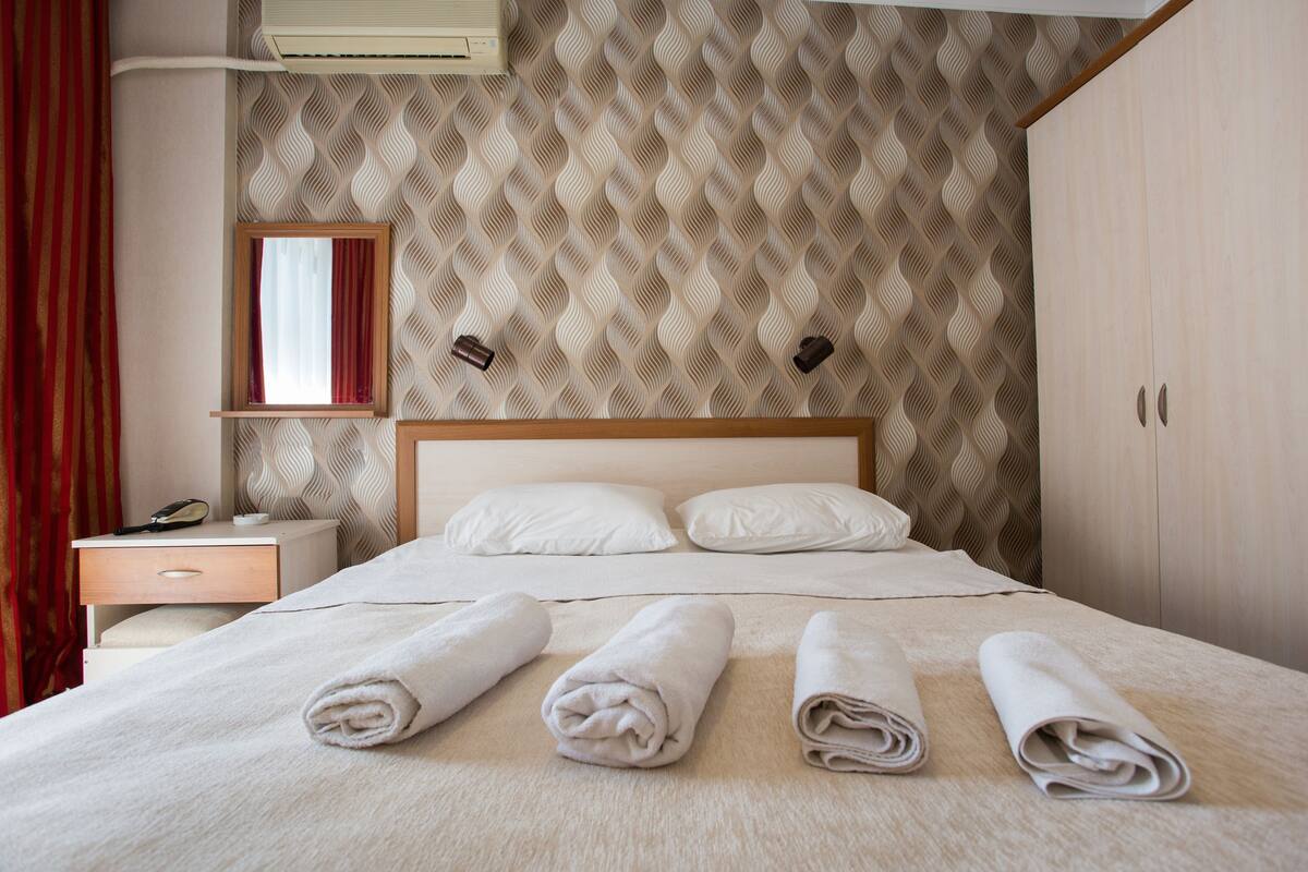 Hotellihuone, jossa on sänky, tyynyjä, yöpöytä, peili ja vaatekaappi.