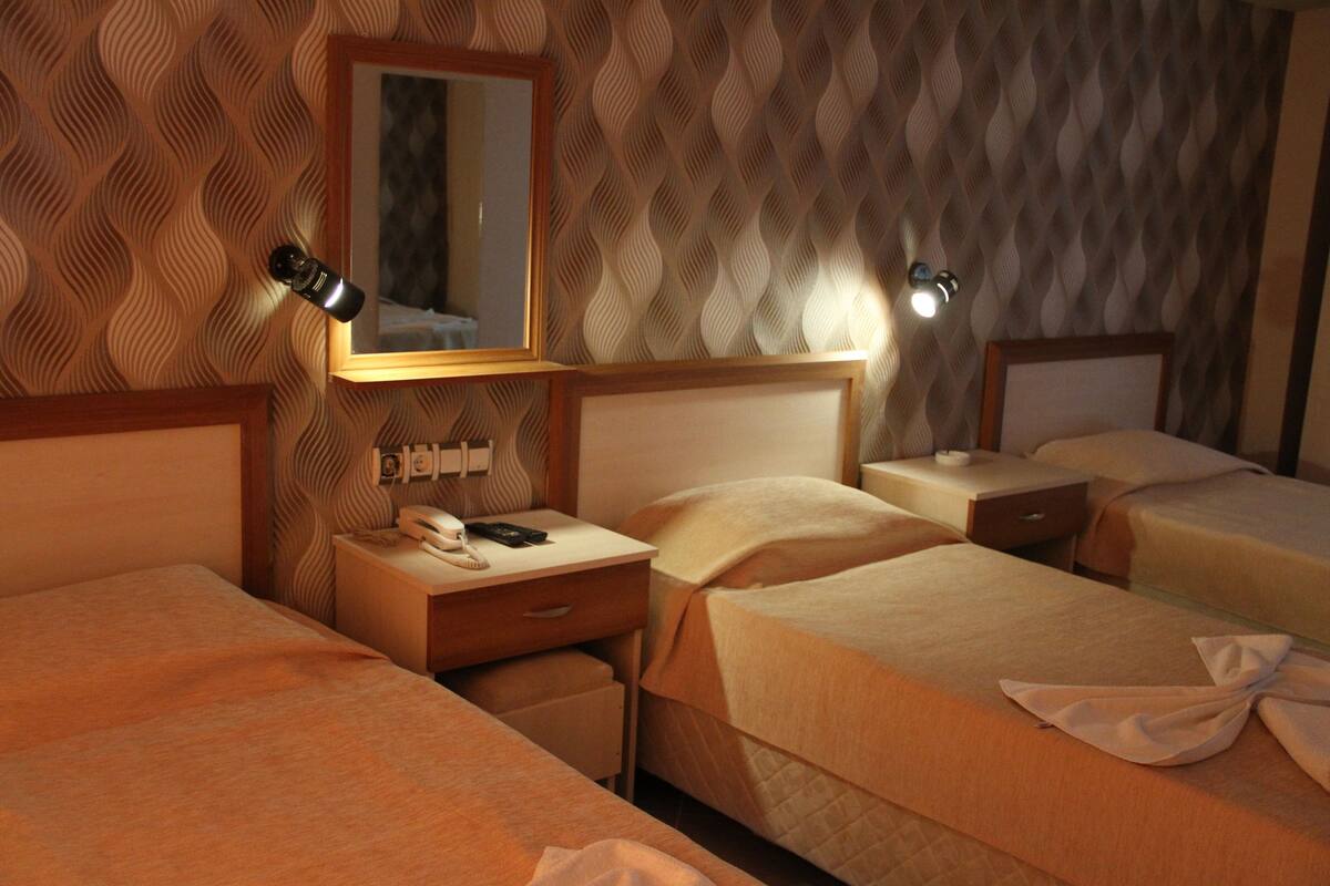 Hotellihuone, jossa on kolme sänkyä, peili, yöpöytävalaisimet, puhelin ja pieni pöytä.