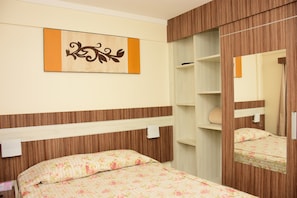 Ein Schlafzimmer mit hölzernem Kopfteil, einem Bett mit floraler Bettwäsche, einem Schrank mit Spiegel und einem an der Wand befestigten Kunstwerk.