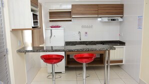A compact kitchen with a granite countertop, two red bar stools, a microwave, a refrigerator, and wooden cabinets. - Reserva Caldas Lacqua 4 (Caldas Novas)