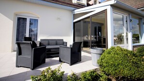 Un patio con mobiliario exterior, un cerramiento de vidrio y un edificio blanco.