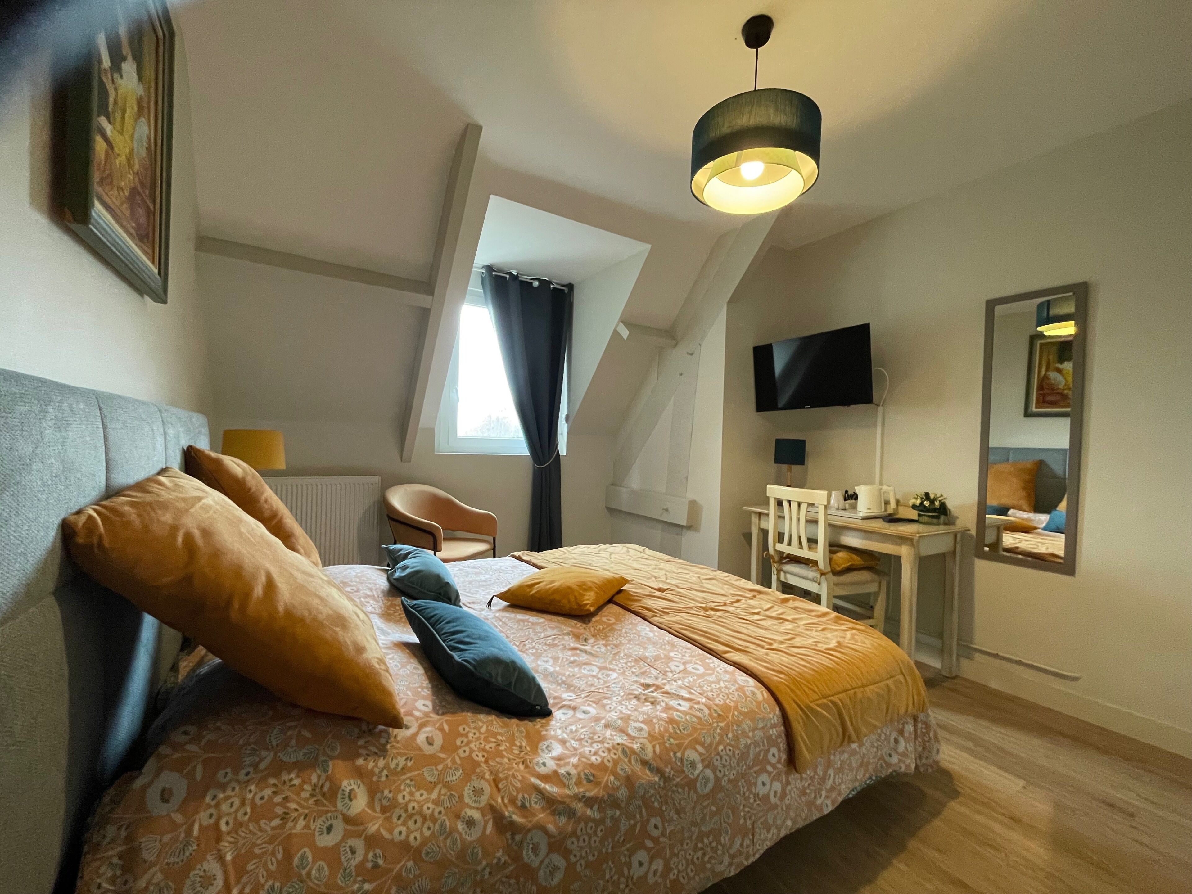 A bedroom with a bed, a desk, a chair, a television, and a window.
