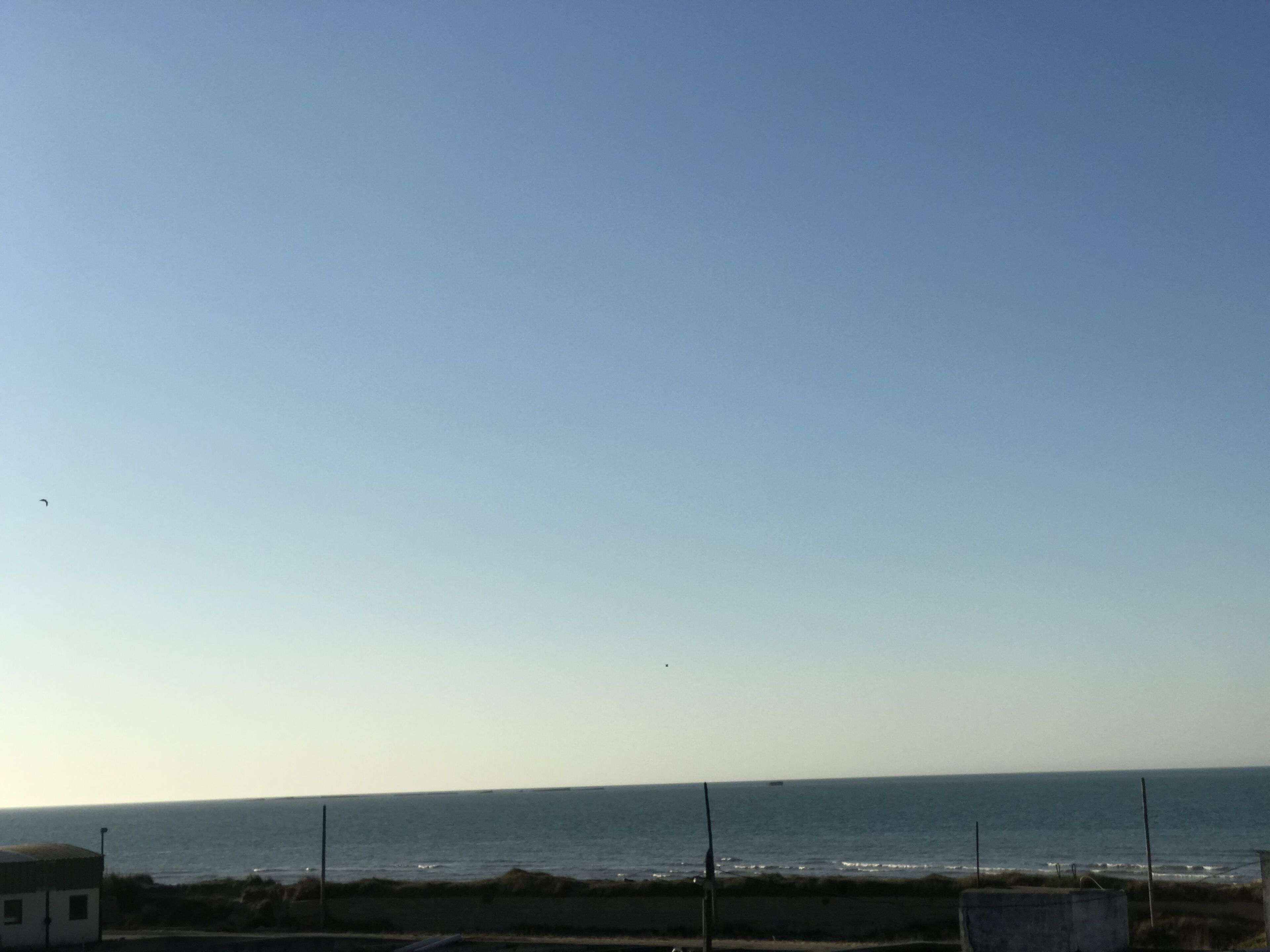 A coastal view with a clear sky, a sandy beach, and a calm sea.