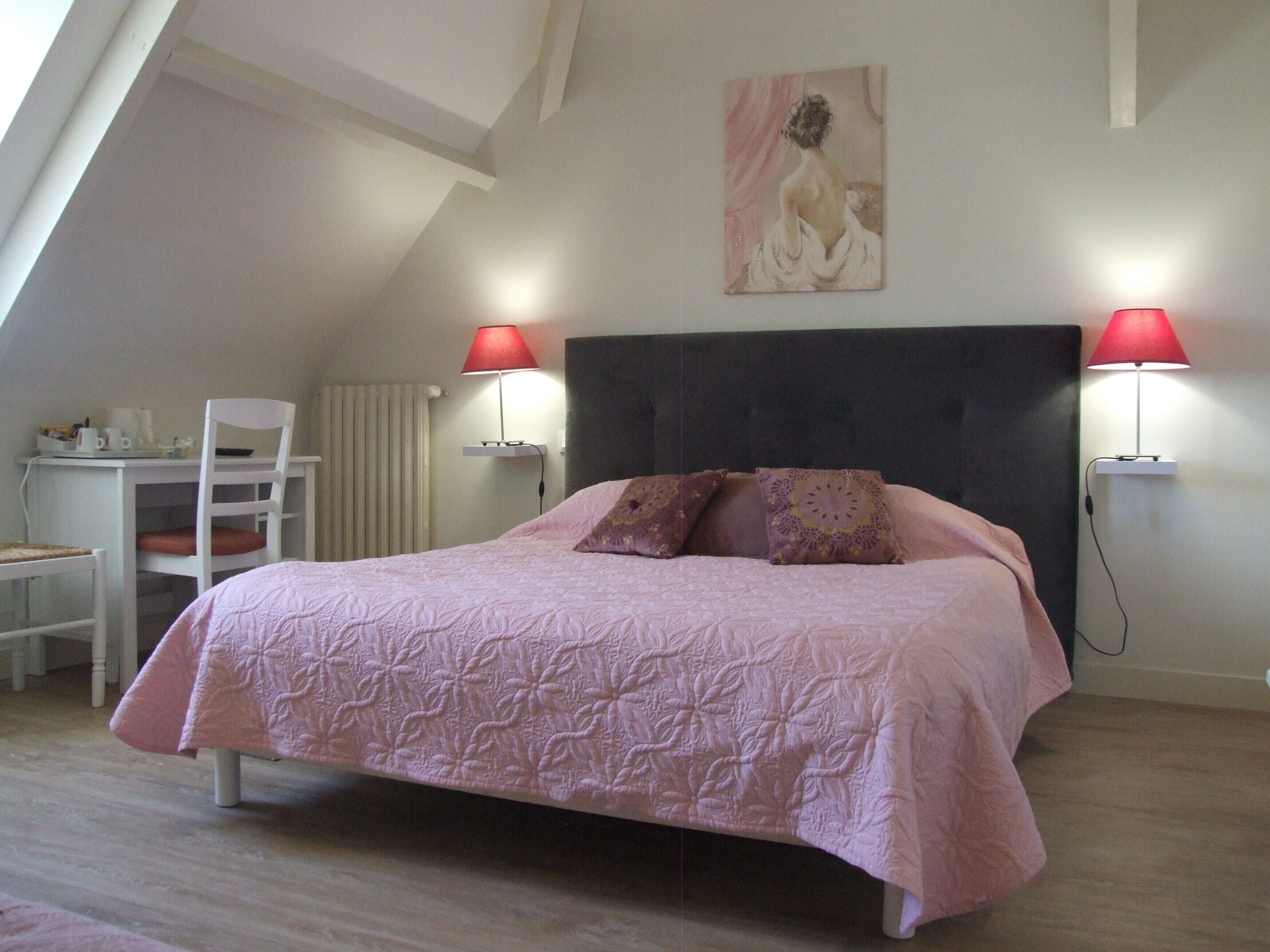 A bedroom with a bed, two bedside lamps, a desk, and a chair.