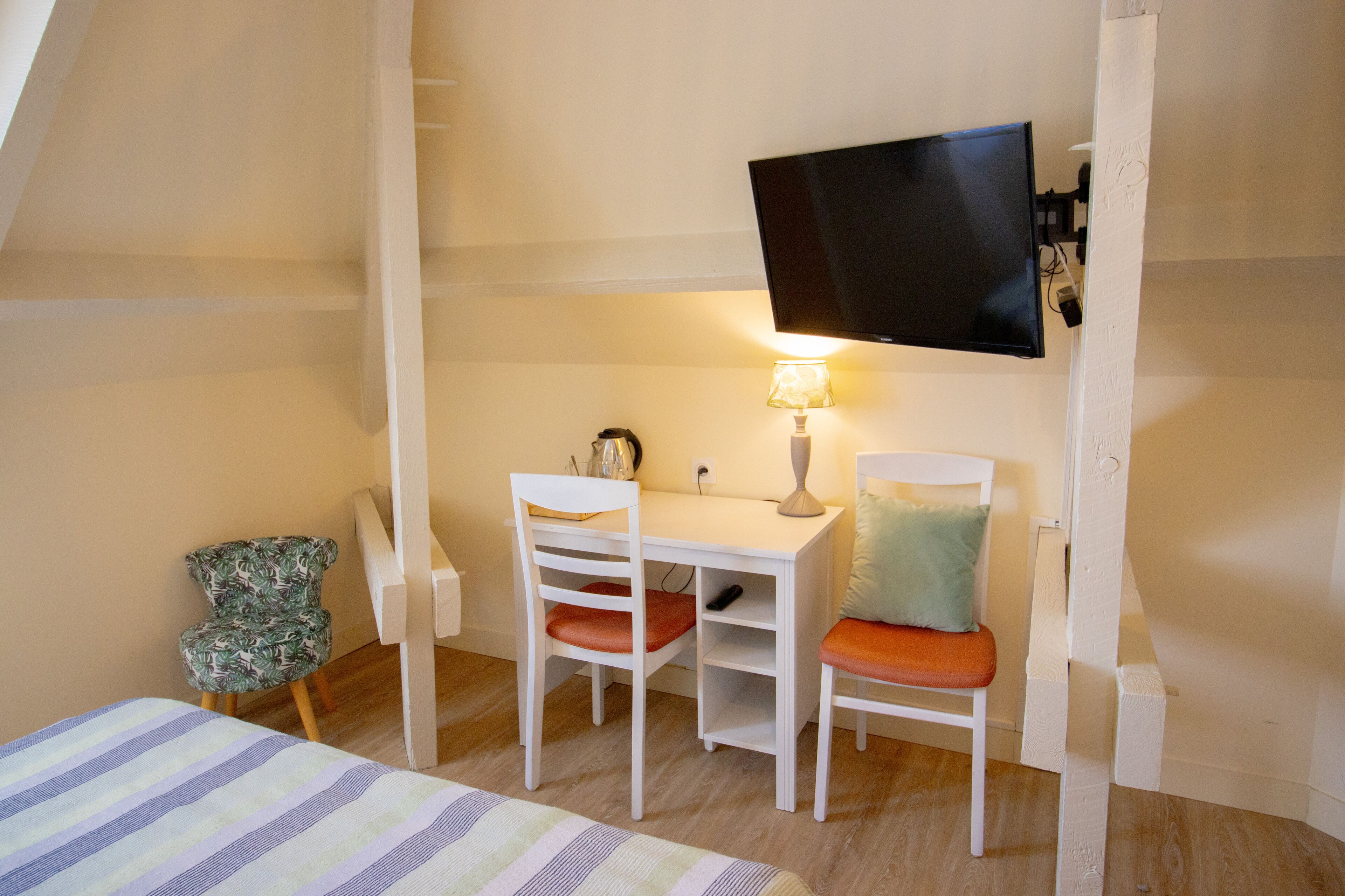 Una habitación pequeña y acogedora con una cama, un escritorio, dos sillas, un televisor y una lámpara.